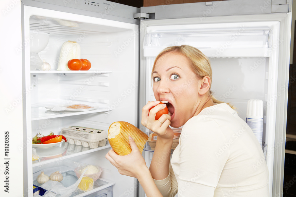 贪婪的女人靠着打开的冰箱吃饭