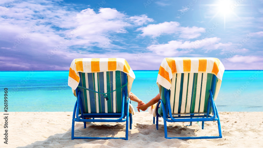 一对夫妇坐在躺椅上在海滩上放松的后视图