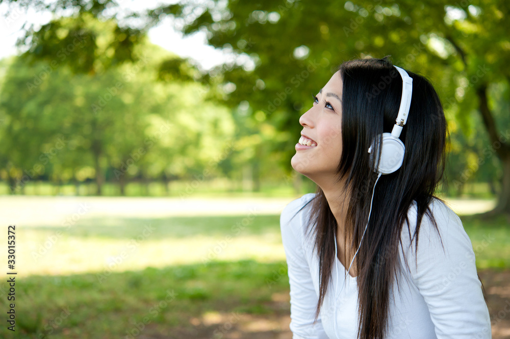 美丽的亚洲女人在公园里听音乐