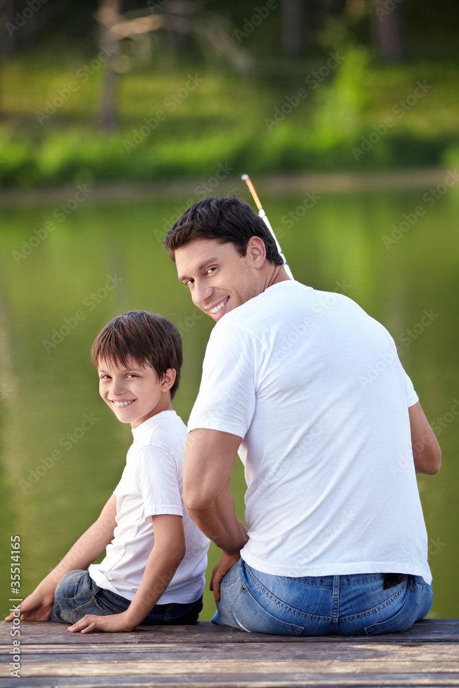 一个男人和一个男孩在湖面上拿着鱼竿