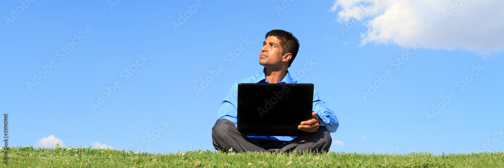 拿着笔记本电脑的商人坐在绿草上仰望蓝天