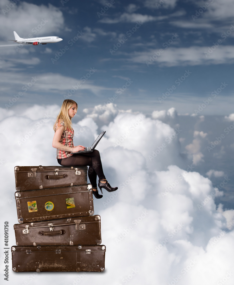 美丽的金发女孩坐在云端的行李箱上