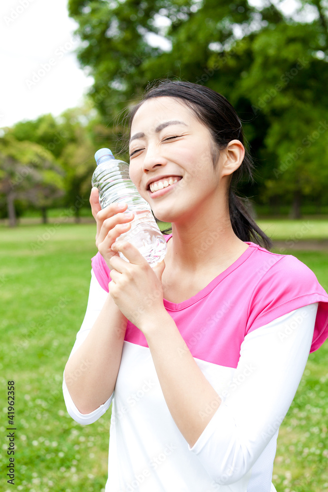 年轻的亚洲女人在公园里喝水