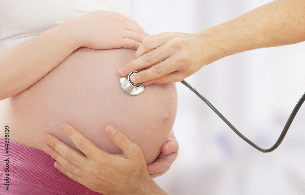 孕妇的肚子和医生用听诊器的手