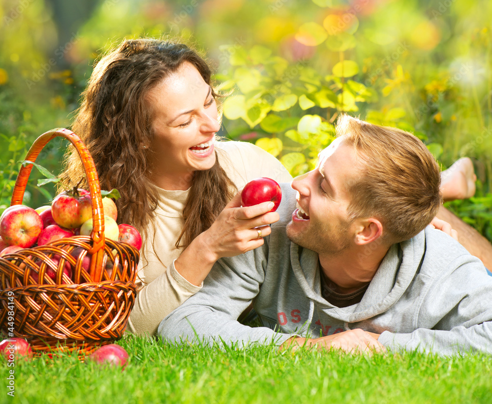 情侣在草地上放松，在秋天的花园里吃苹果