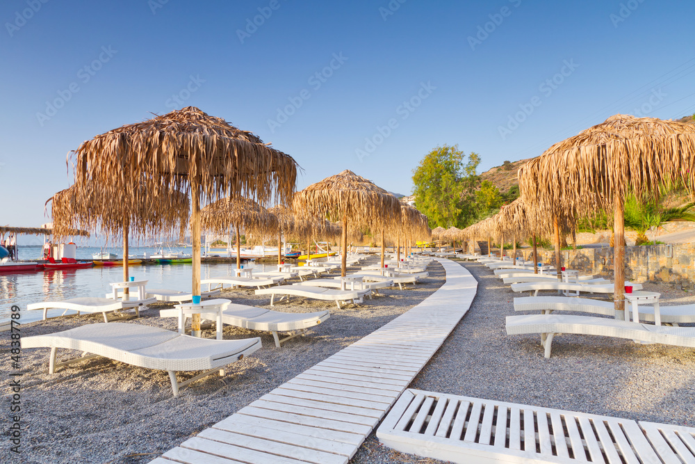 希腊克里特岛公共海滩遮阳伞下的日光浴床