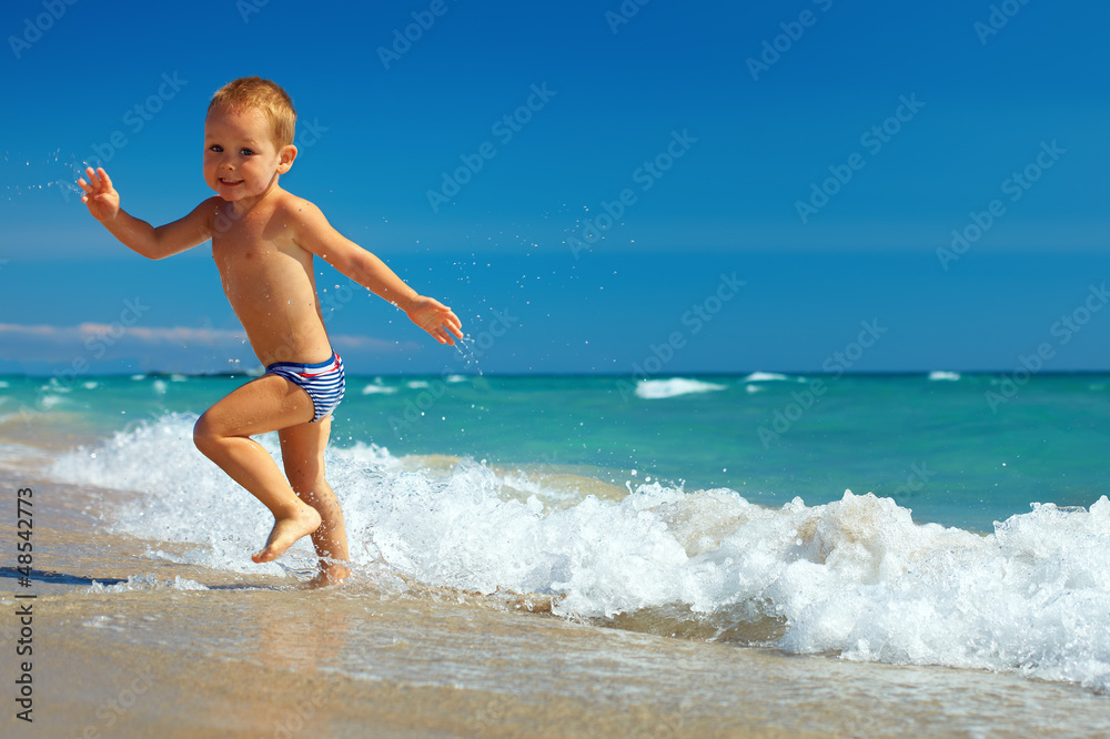 快乐的婴儿在海滩上从冲浪中奔跑