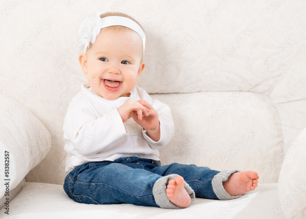 快乐的小女婴穿着牛仔裤坐在沙发上大笑