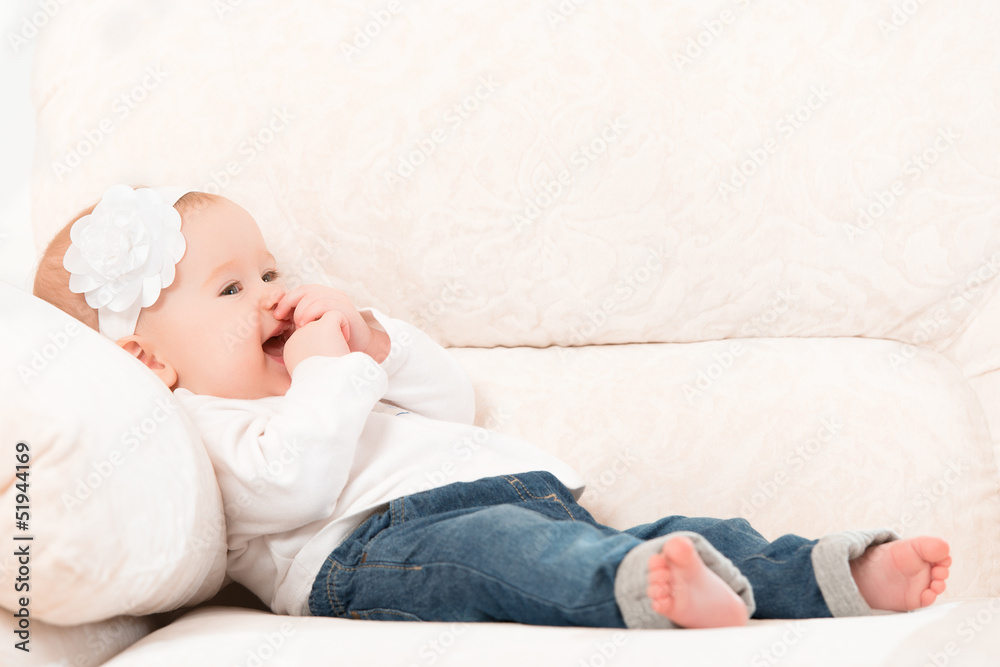 快乐的小女婴穿着牛仔裤坐在沙发上大笑