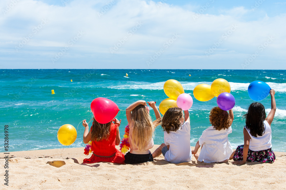孩子们拿着彩色气球坐在海滩上。