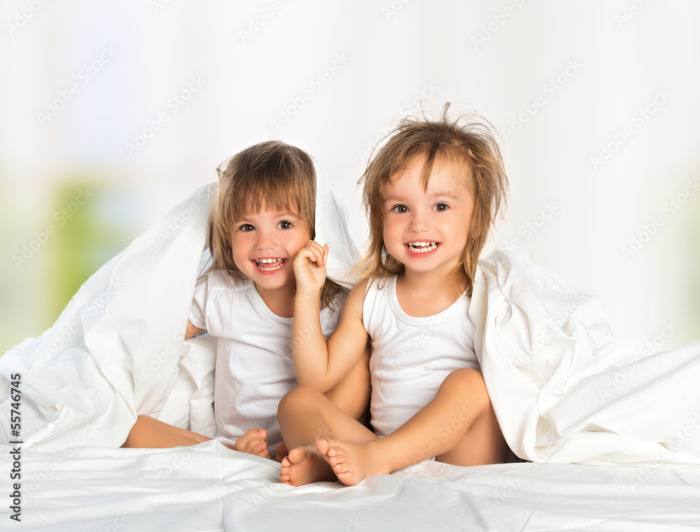 happy little girl twin sister in bed under the blanket having