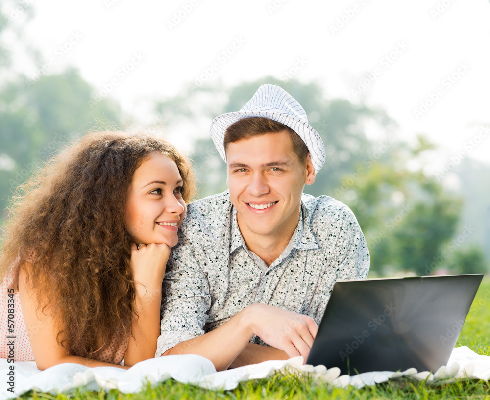 一对夫妇带着笔记本电脑躺在公园里