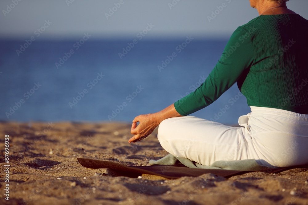 Mature woman doing yoga on sandy beach