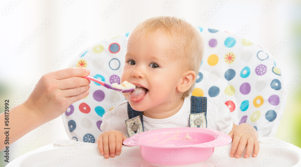 happy mother feeds funny  baby from  spoon