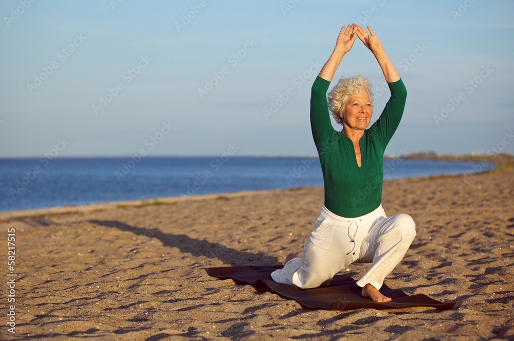 成熟的女人在海滩上伸展身体-瑜伽