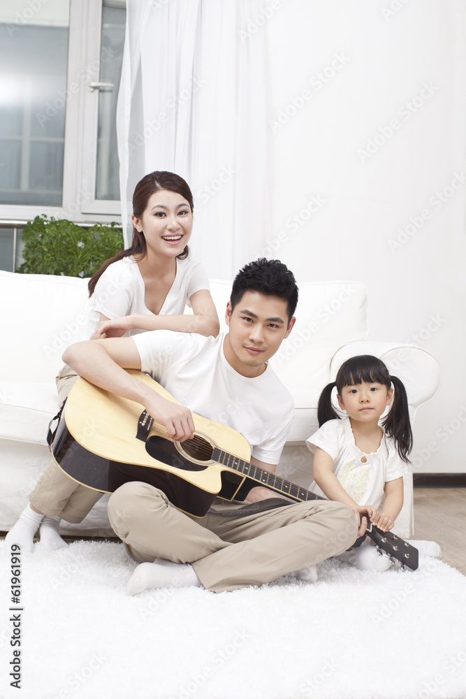 。年轻的一家人在客厅里弹吉他。