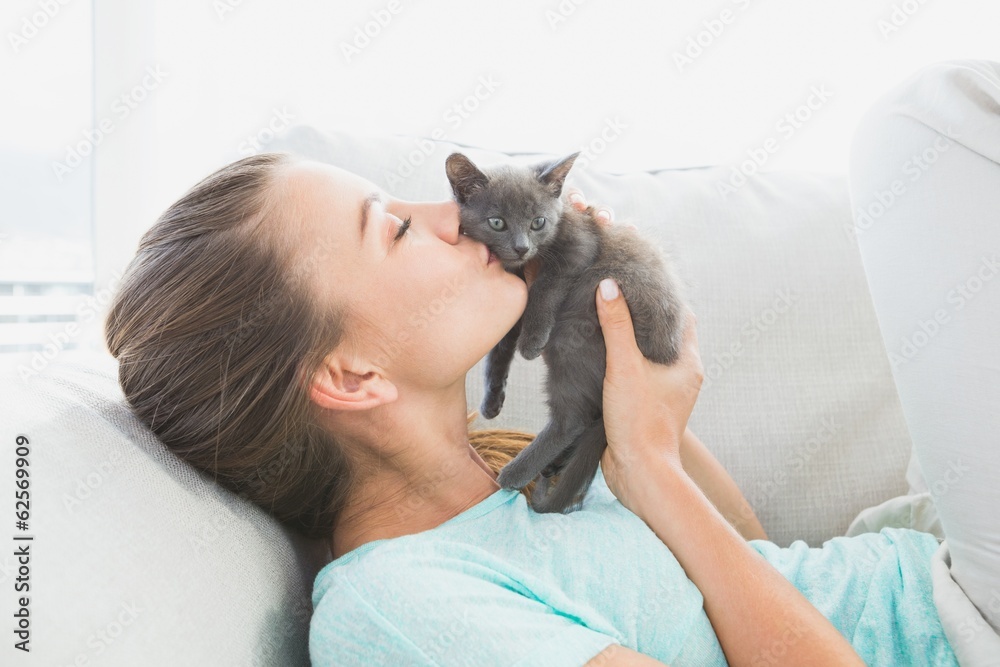 躺在沙发上亲吻灰色小猫的快乐女人