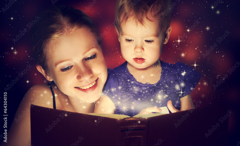 母亲和孩子宝贝女儿在黑暗中阅读魔法书