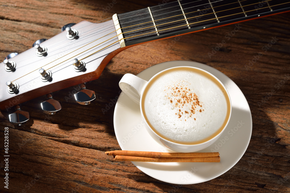 A cup of cappuccino and guitar on wooden table