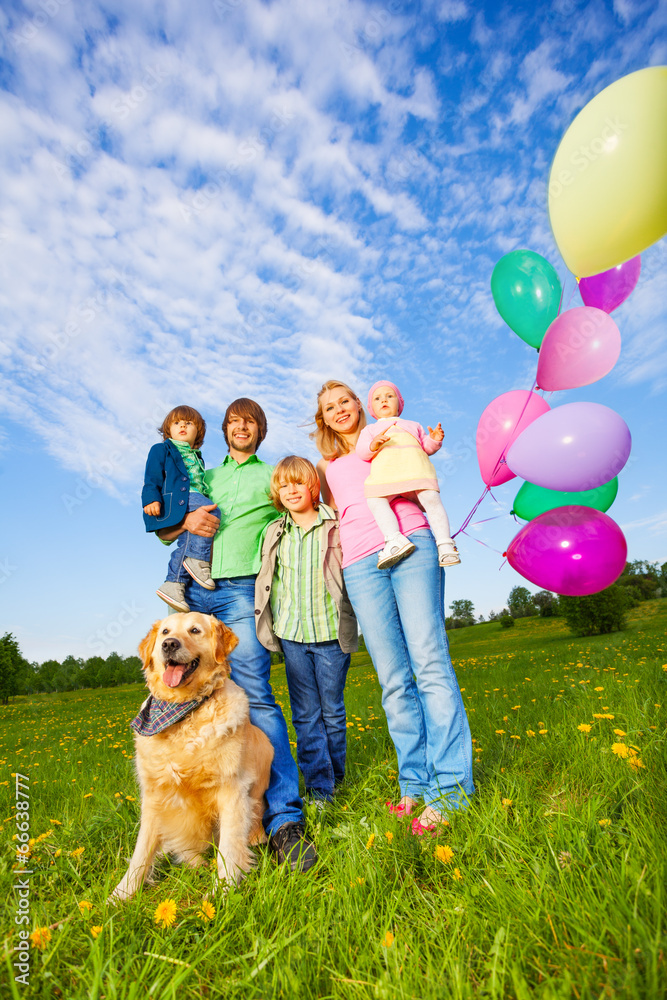 Parents, kids and dog stand with balloons in park
