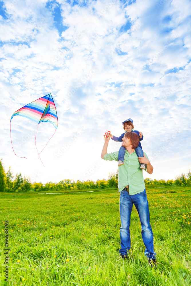 Smiling father holds kid and watches kite in air