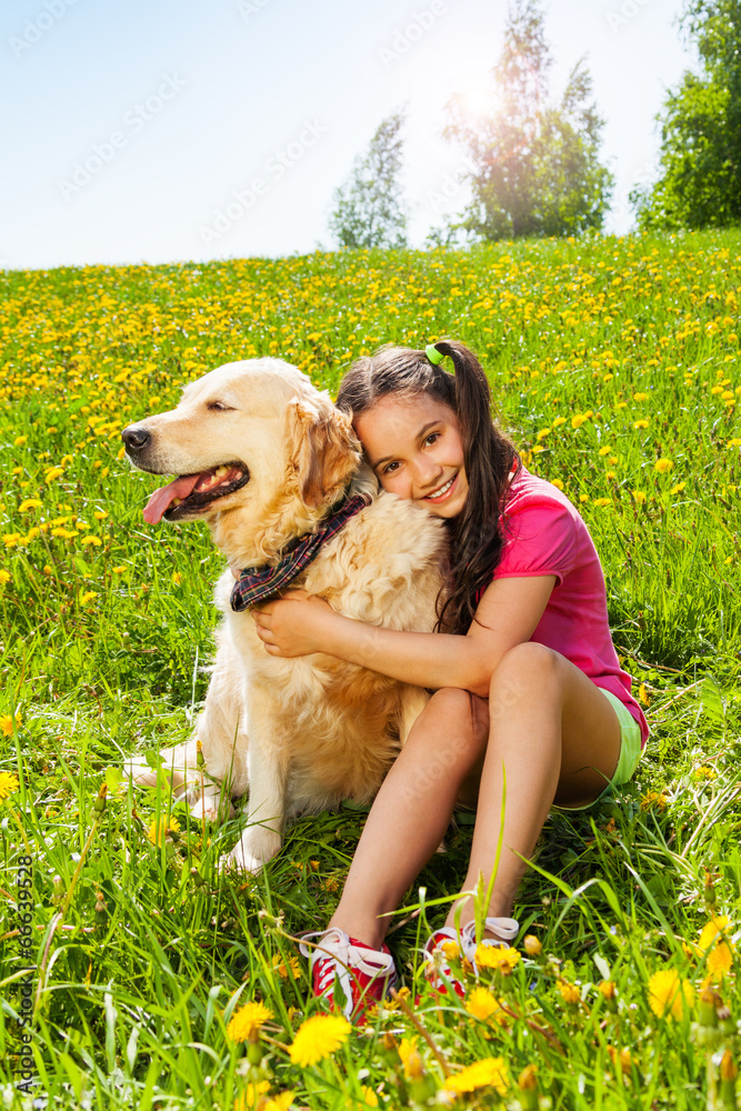 微笑的女孩拥抱坐在草地上的可爱小狗
