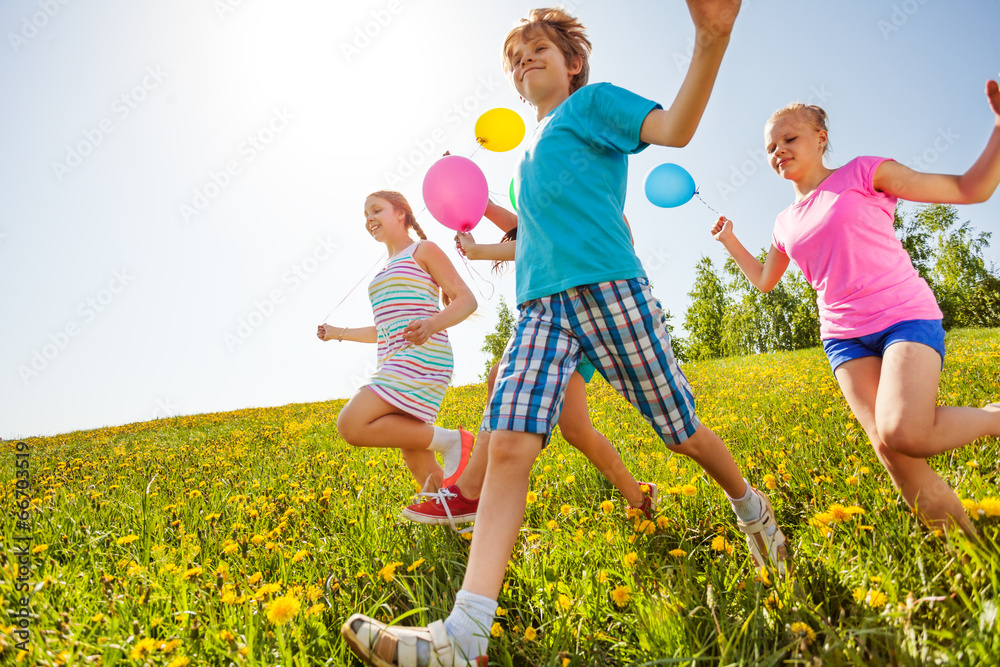 Happy children with balloons run in green field
