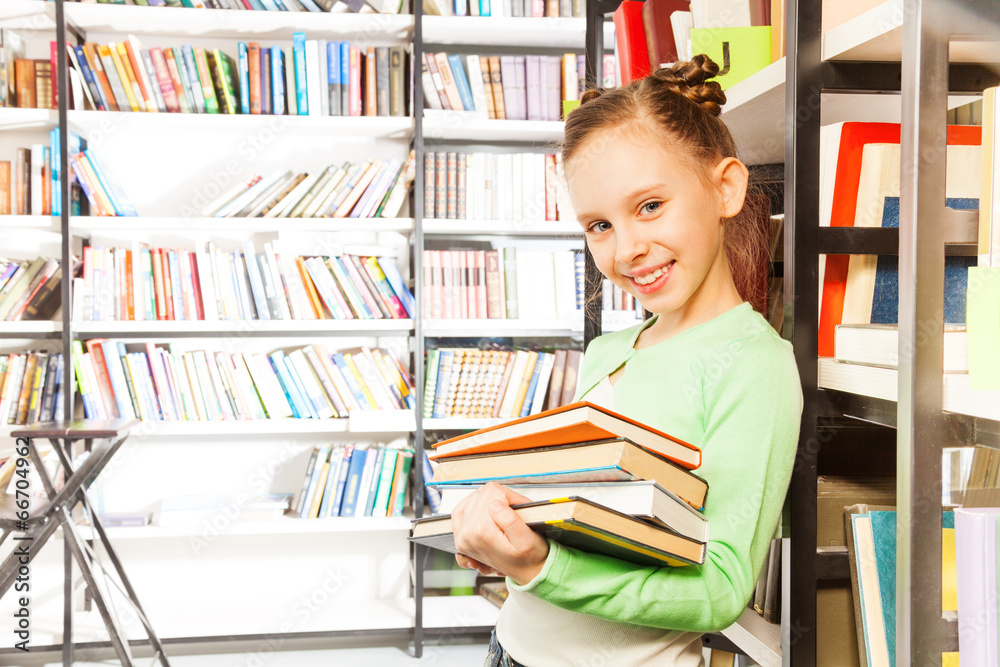 Schoolgirl smiles and holds books in library