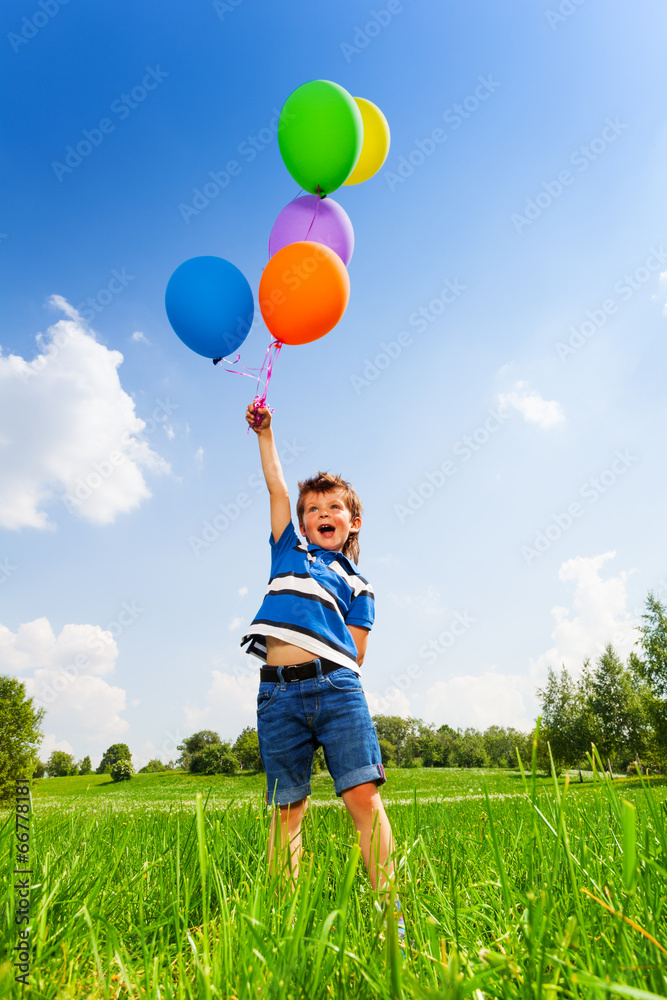 绿色公园里带着五颜六色气球的兴奋男孩
