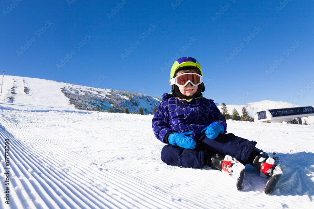 戴着滑雪面罩的小男孩坐在雪地上