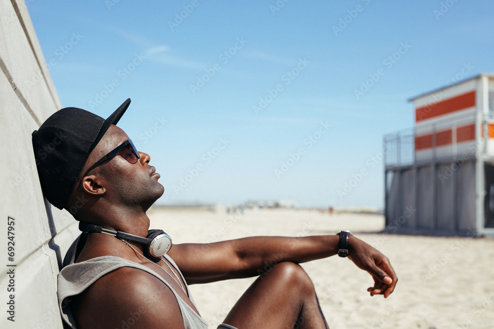 放松的非洲男子靠在海滩的墙上