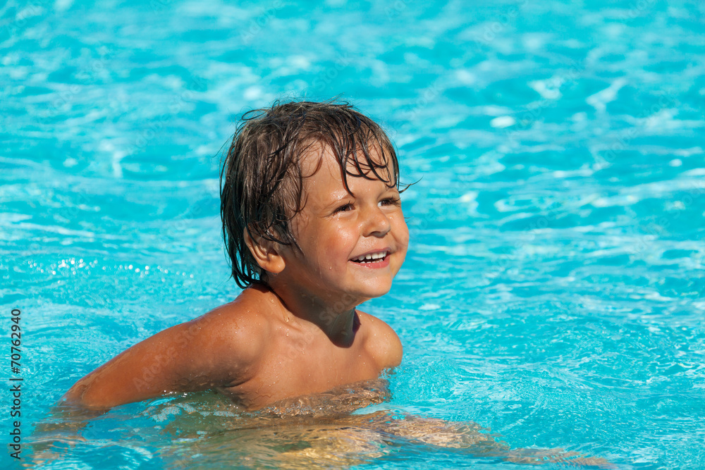 微笑的男孩在游泳池里游泳，看着