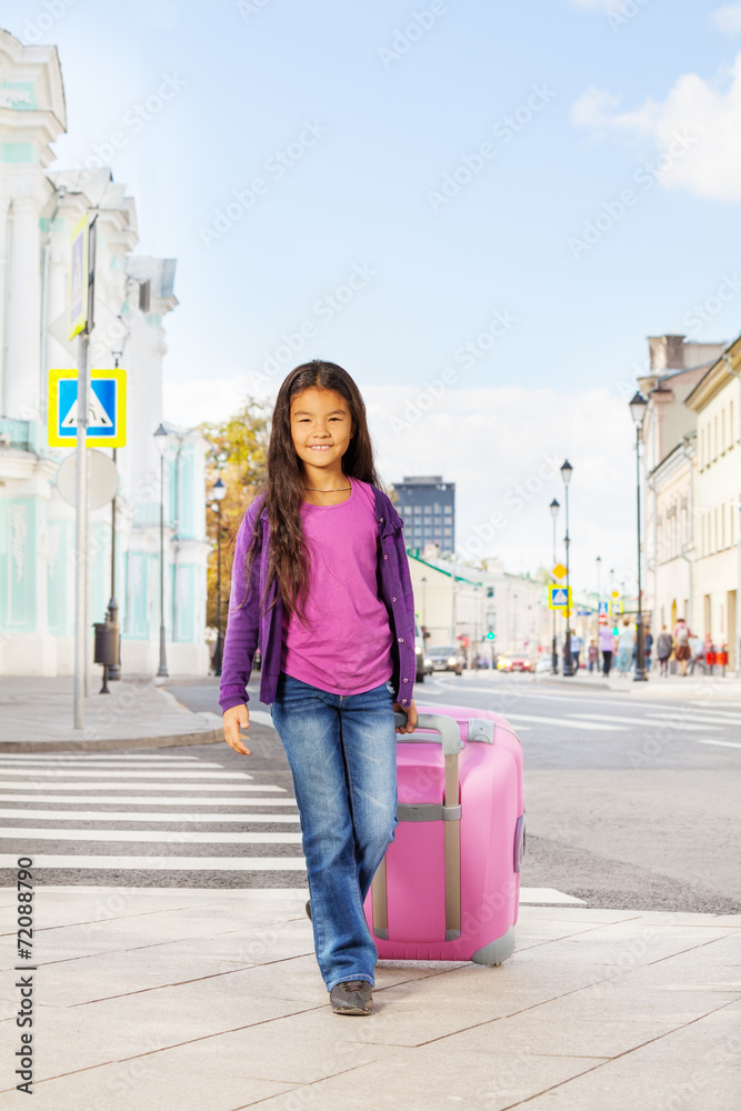 亚洲小女孩在街上拿着粉红色的行李