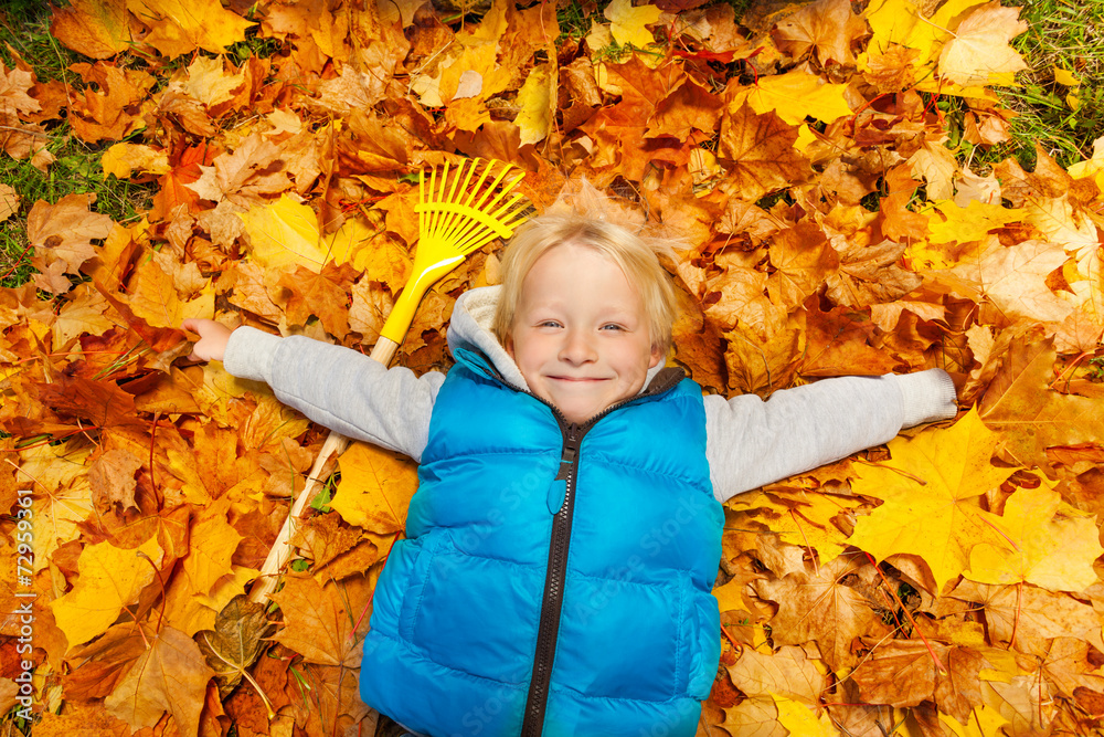 快乐的金发男孩躺在秋叶上