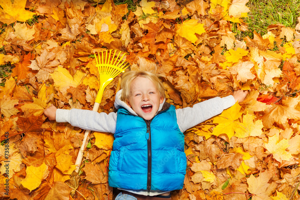 笑男孩用耙子躺在秋叶上