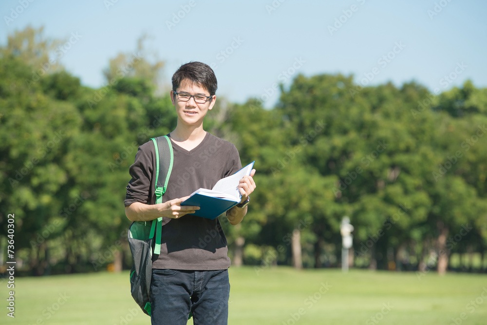 英俊的男孩拿着一本打开的书，阅读背景是夏天的绿色