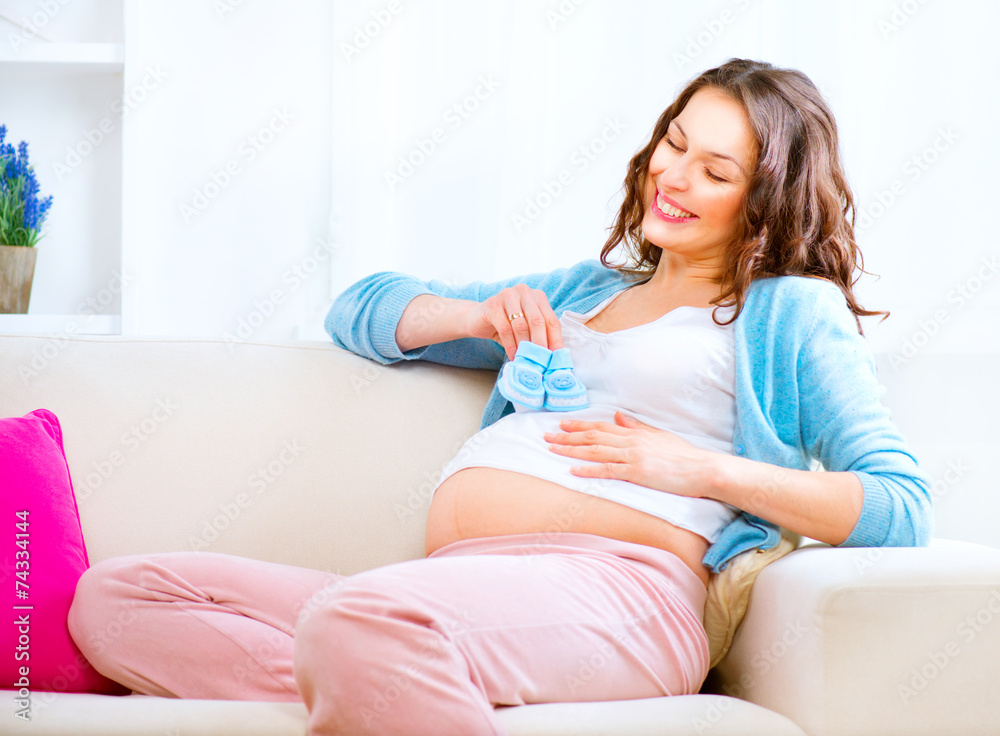怀孕快乐的女人手里拿着蓝色婴儿鞋