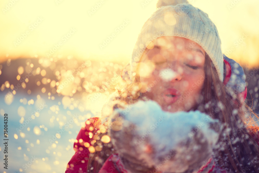 美丽的冬日女孩在霜冻的公园里吹雪。阳光明媚