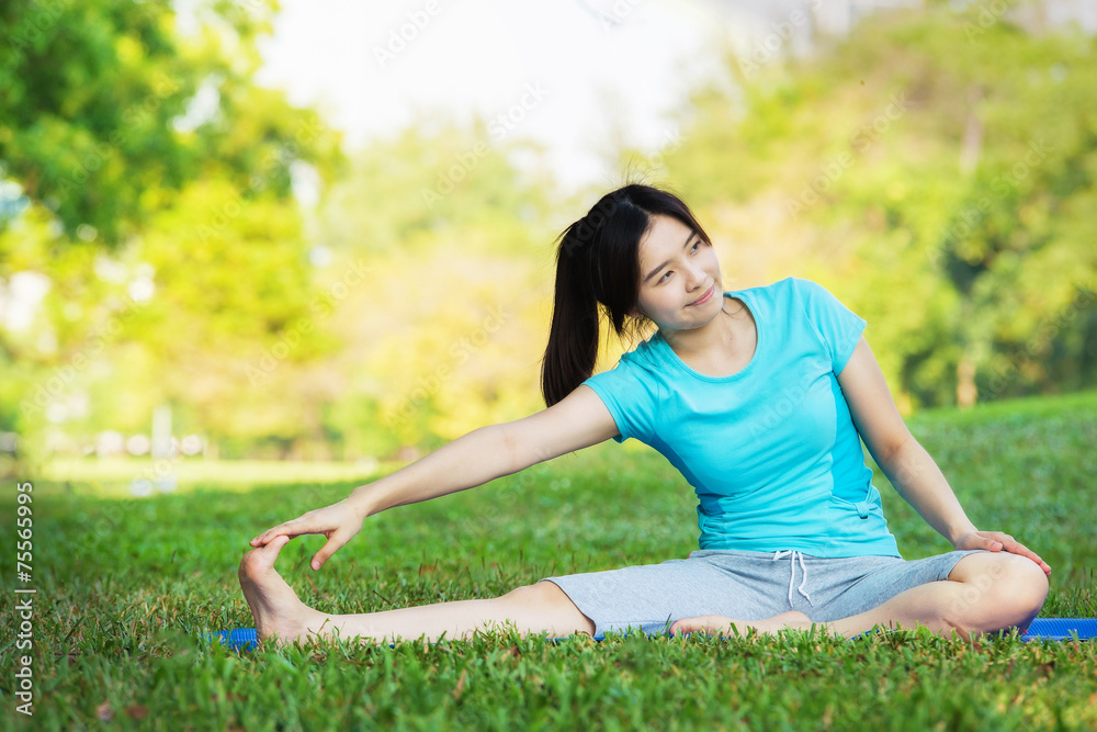 Young woman doing yoga exercise on green grass