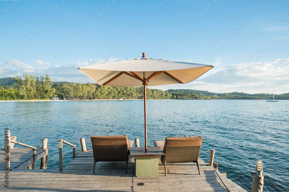蓝天下，两把椅子、沙滩和木桌子上的雨伞。苏