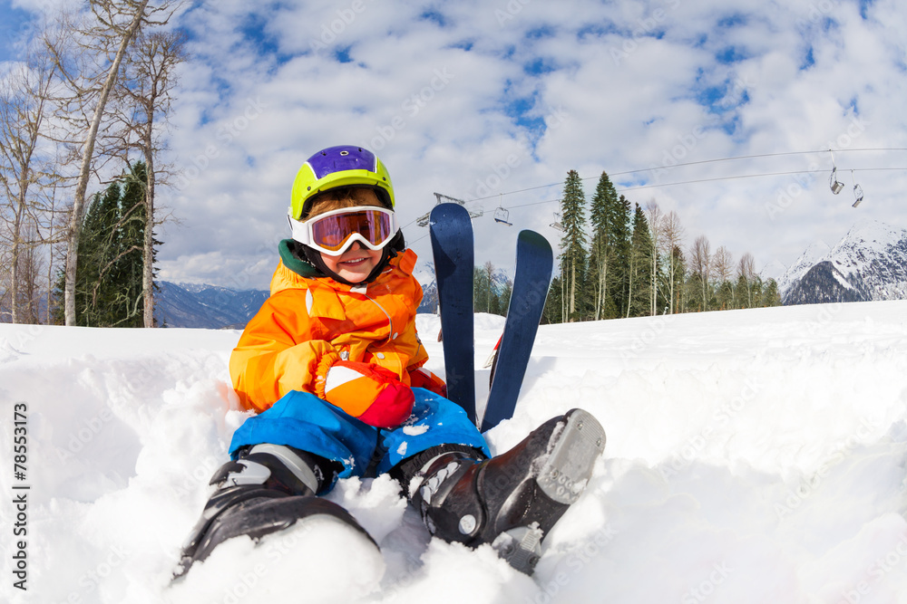 戴着滑雪面罩和头盔坐在雪地男孩身上
