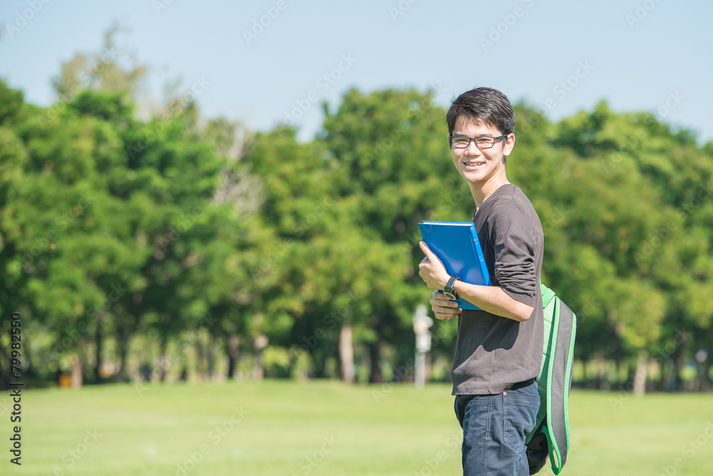 亚洲学生拿着书站在公园a微笑