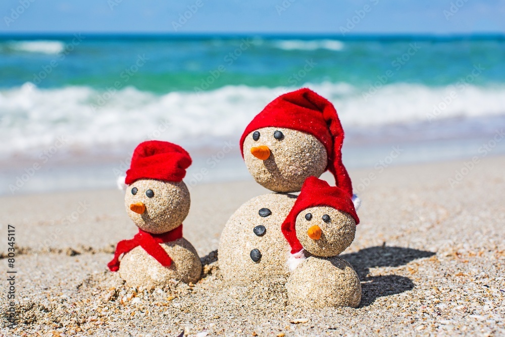 海滩。戴着圣诞老人帽的海滩上的雪人一家。新年和
