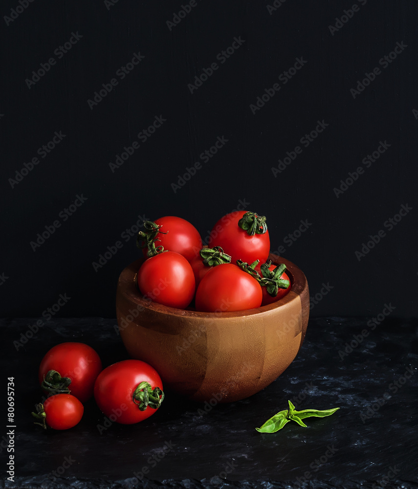 Ripe cherry-tomatoes in wooden bowl with basil leaves