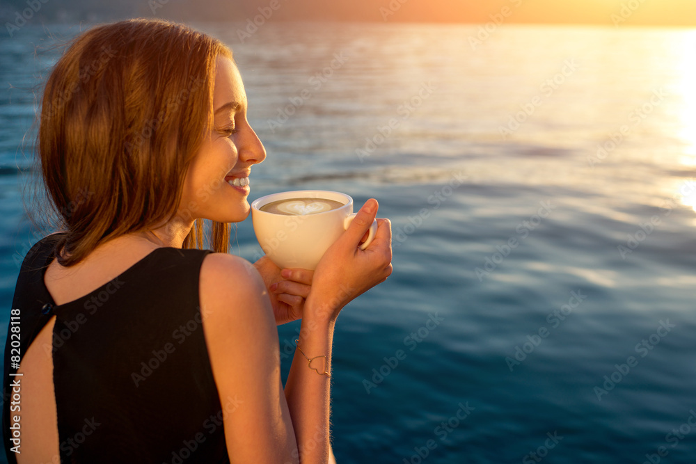 日出时年轻女子在码头上喝咖啡