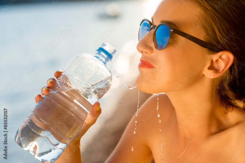 在海滩上用透明瓶喝水的女人