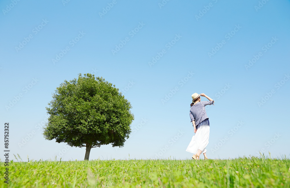 一本木のある原っぱを散歩する女性