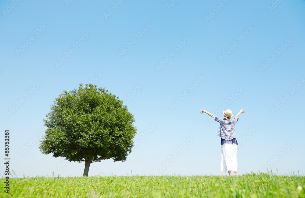 一本木のある原っぱで手を広げる女性