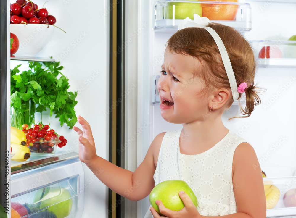小女孩拿着水果在冰箱旁哭泣和表演