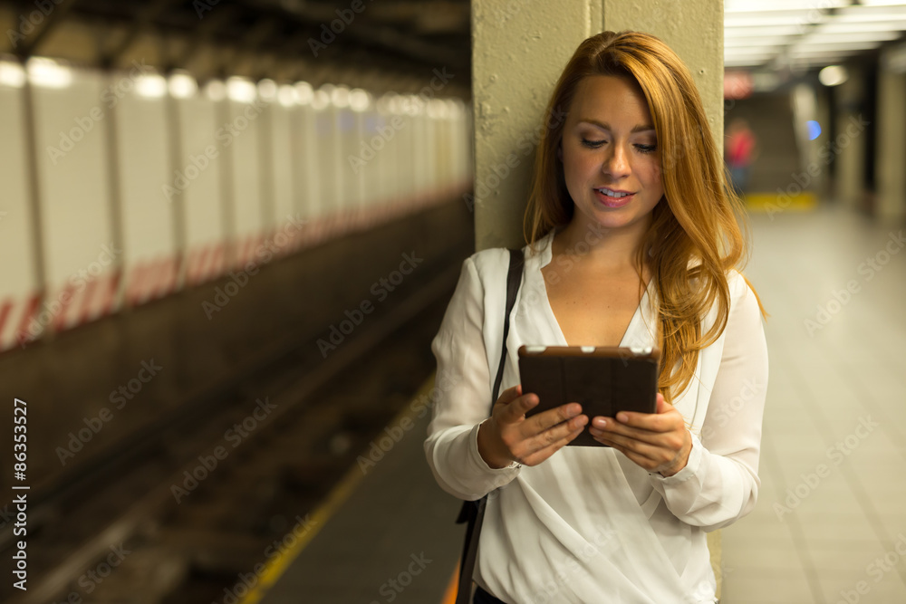 城市中年轻的高加索女性在地铁站台使用平板电脑